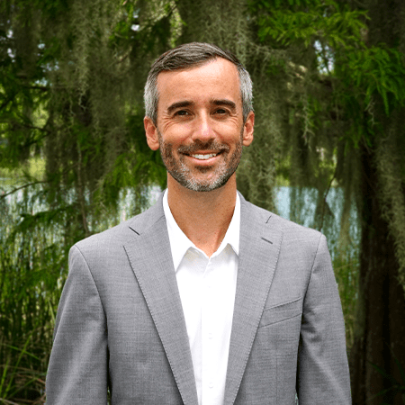 photo of Joel Gordon, agent, in a grey suit in front of Park Lake in Orlando Florida